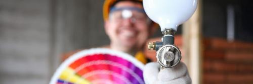 Smiling builder shows spray gun and color swatches